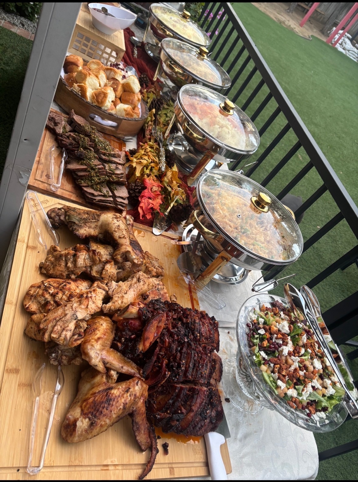 A catered spread with grilled meats, salad, sides, and chafing dishes